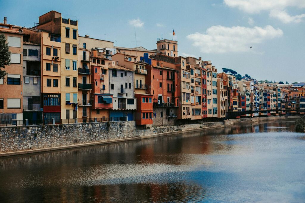 Vibrant apartment facades line the Onyar River in Girona, Spain, reflecting architectural beauty.